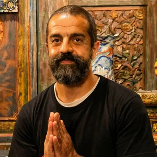 Ali Taghavi with palms together in prayer before carved Balinese wood panels