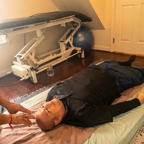 Client resting on a treatment table while a practitioner works at the head