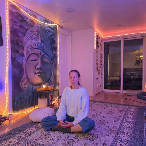 Young woman meditating cross-legged in a softly lit violet room