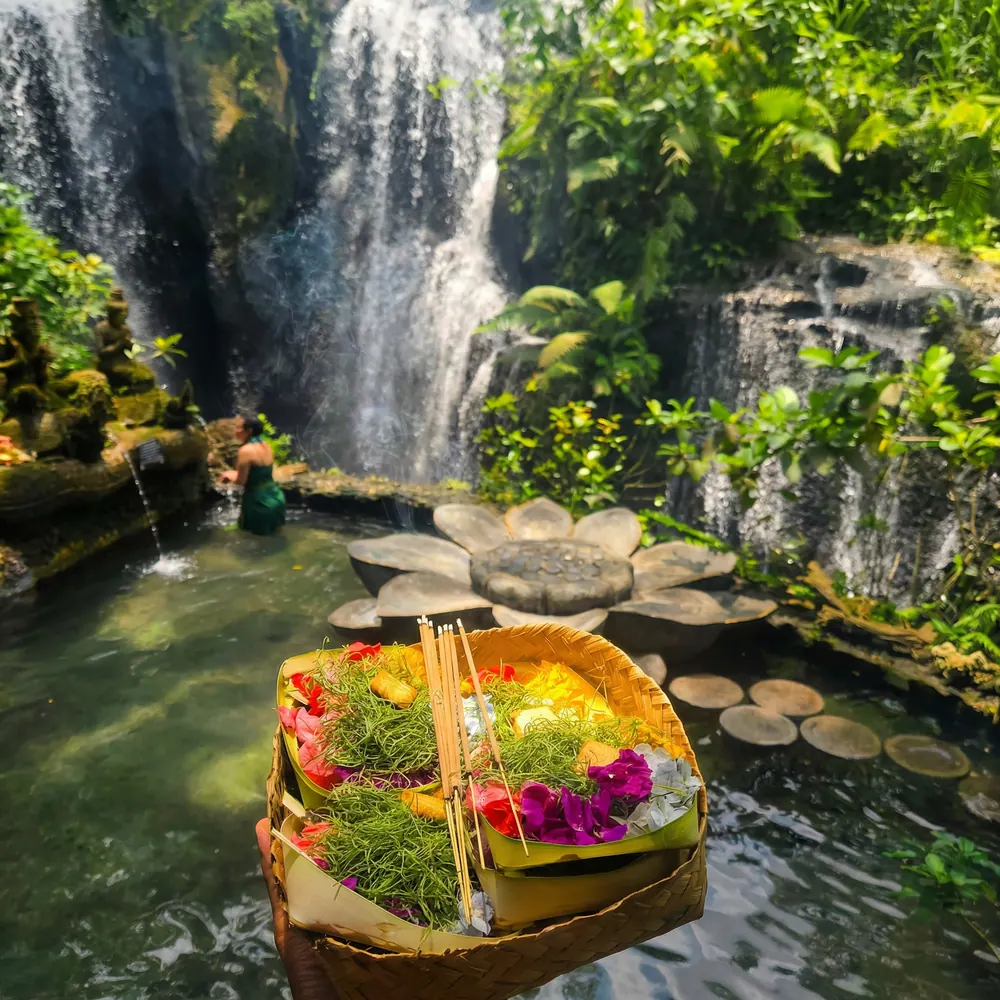 Woven flower offering floating in a garden pool below a waterfall