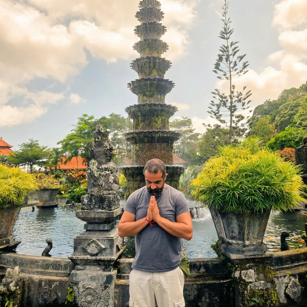 Man with palms together beside a tiered water-temple fountain