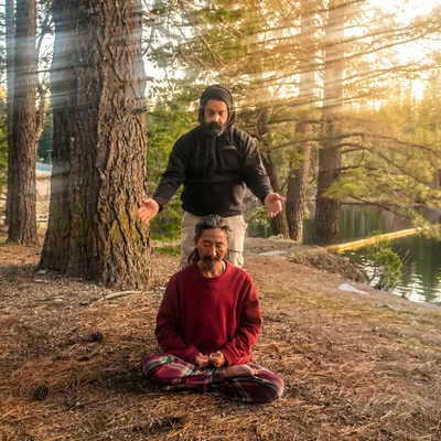 Outdoor session in a sunlit forest, one man seated in meditation