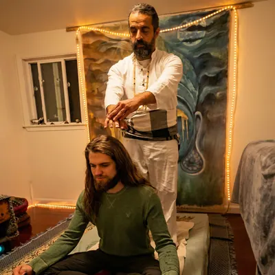 Ali holding his hands above a young man seated on the floor