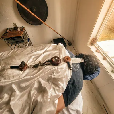 Client lying under a blanket with singing bowls placed on the body